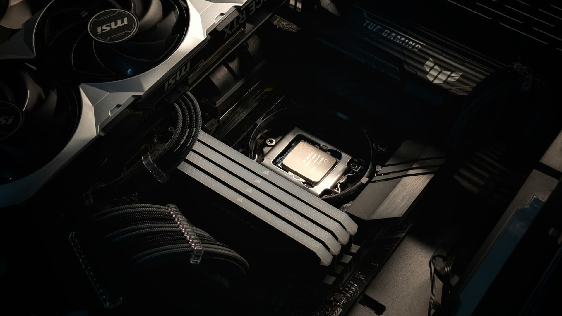 Interior of a PC case showing an MSI RTX GPU in the PCIe slot, four Corsair RAM sticks installed in DIMM slots, and an Intel CPU seated in the socket on an ASUS TUF Gaming motherboard